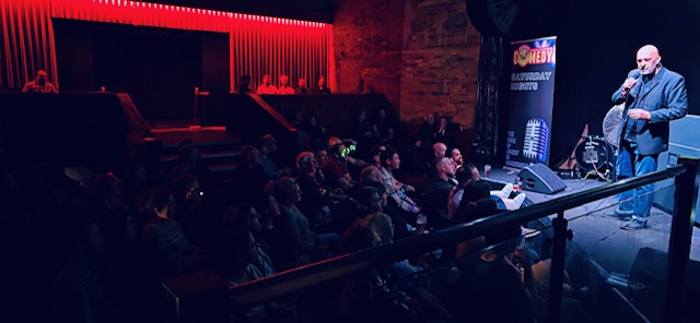 Comedian entertaining packed crowd under atmospheric red lighting at Bournemouth comedy night